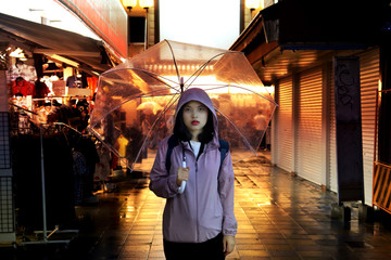 Backpack teen lady hold  transparent umbralla on streel in rainy night.