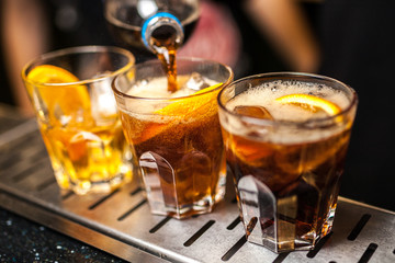Close-up of expert bartender making cocktail in bar, splash of whiskey and cola.