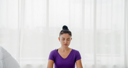 Fototapeta na wymiar A beautiful young woman sitting in a yoga room in a calm and relaxed manner. Light, comfortable, light window background comes in the morning. Health care concepts