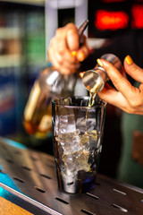 Close-up of expert bartender making cocktail in bar, splash of whiskey and rum.