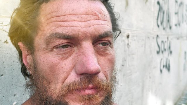 Slow motion close-up face of real homeless man. Real person with no fixed abode. Down-and-out person on the street. Degraded man looks at the camera, social degradation