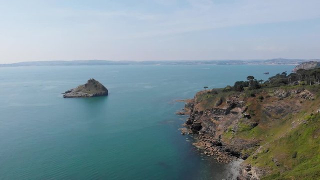 An aerial forward footage of a rocky island rock (Thatcher Point) along rocky cliff and turquoise water under a majestic blue sky