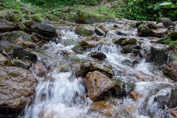 mountain river with large stones in the riverbed and stone banks, surrounded by forest along the banks, on a bright sunny day, with clouds in the sky.