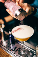 Bartender finishes preparation of cocktail in crystal glass by adding a bitter of powdered sugar. Close-up of expert bartender making cocktail in bar.