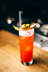 Close-up orange cocktail with olives on the bar, blurred background.