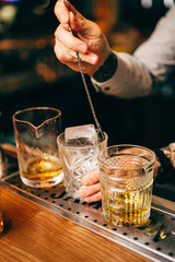Close-up of expert bartender making cocktail on the bar, blurred background.