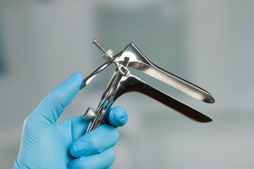 doctor's hand in medical gloves holds a medical speculum