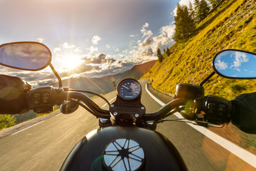 Motorcycle driver riding in Alpine highway, handlebars view, Austria, Europe.