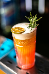 Close-up orange cocktail with dried lemon and rosemary on the bar, blurred background.