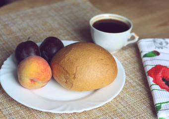 Homemade breakfast, cup of coffee, bun and fruit on a plate, peach and plums, white napkin with red poppies