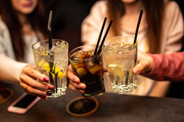 Close up of girls drinking cocktails in nightclub. Girls having good time,cheering and drinking cold cocktails, enjoying friendship together in bar, close up view on hands.