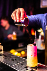 Bartender finishes preparation of cocktail in crystal glass by adding a bitter of cinnamon. Close-up of expert bartender making cocktail in bar.