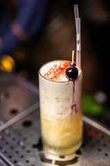 White cocktail with foam and cocktail cherry on the bar