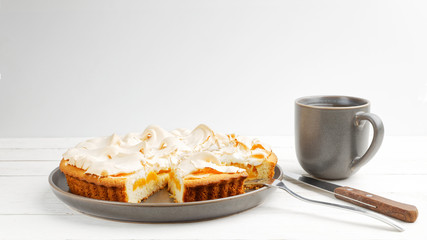 Homemade apricot pie decorated with meringue and a mug of tea on a white wooden table. Copyspace.