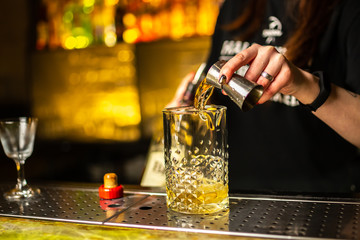 Close-up of expert bartender making cocktail on the bar, blurred background.