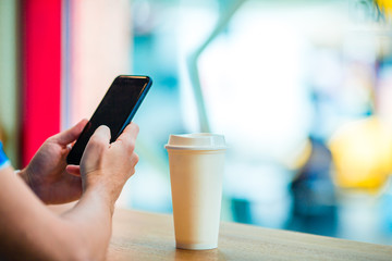 Closeup of male hands holding cellphone and glass of coffee in cafe.