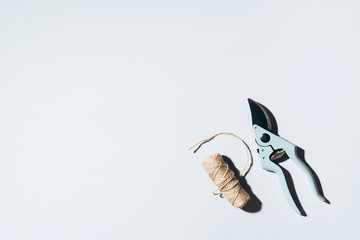 Branch pruner and craft linen threads over grey background. Gardening tools. Spring still life.