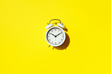 White alarm clock with hard shadow on yellow background. Top view. Wake up alert concept. Morning routine.