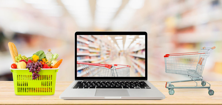 supermarket aisle blurred background with laptop computer and shopping cart on wood table grocery online concept