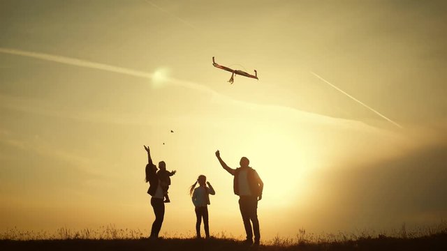 Happy family playing with a kite while on meadow, sunset, in summer day. Funny family time. Happy little girl launch a kite with parents. Mom, Dad and daughter are happy together.