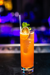 Close-up orange lemonade cocktail with mint and dried lime on the bar, blurred background.