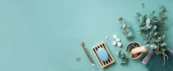 Fotobehang Soap, eucalyptus, towels, massage brush, salt, aroma oil and other spa objects on green background. Top view. Skin care, body treatment concept. Banner. © jchizhe