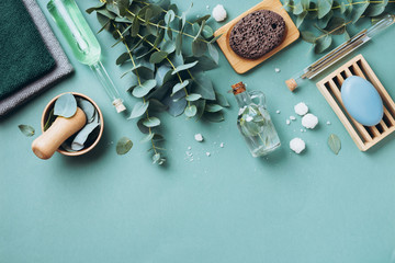 Soap, eucalyptus, towels, massage brush, salt, aroma oil and other spa objects on green background. Top view. Skin care, body treatment concept. Banner.