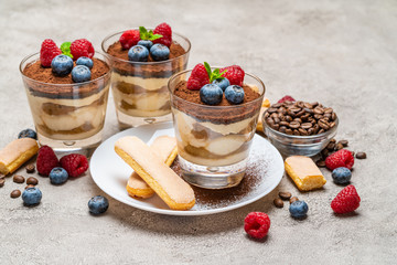 Classic tiramisu dessert with blueberries and raspberries and savoiardi cookies in a glass on concrete background