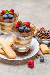Classic tiramisu dessert with blueberries and raspberries and savoiardi cookies in a glass on concrete background