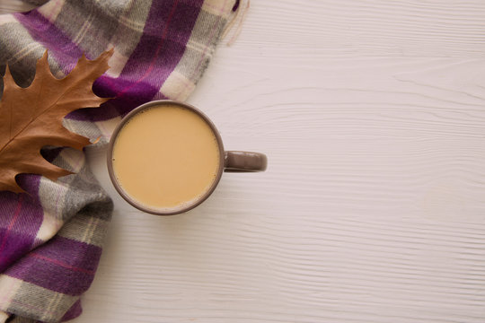 Autumn concept. A cup of warm cocoa, dried leaves and woolen scard of white background. Copy space. 