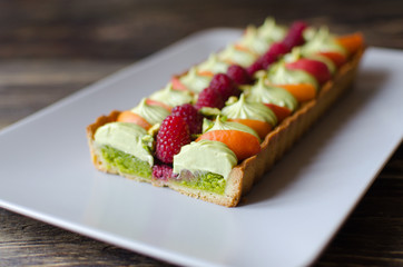 Homemade pistachio tart with fresh raspberries and apricot on dark wooden background