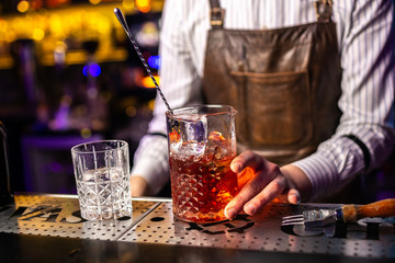 Close-up of expert bartender making cocktail on the bar, blurred background.