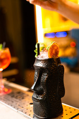 Cocktail in black glass with dried orange and mint on the bar, blurred background.