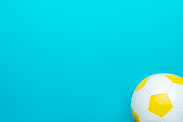 Top view of part of white and yellow soccer ball over turquoise blue background with copy space....