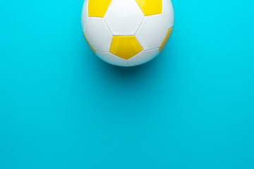 Top view of part of white and yellow soccer ball over turquoise blue background with copy space. Minimalist flat lay image of football ball as sport background.