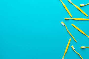 Top view photo of many new yellow toothbrushes over turquoise blue background with copy space. Flat lay image of manual plastic toothbrushes with right side composition.