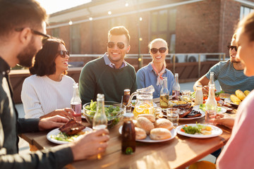 leisure and people concept - happy friends having dinner or bbq party on rooftop in summer