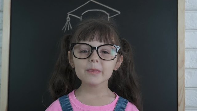 Smile with graduated cap. A smart little girl in glasses and a master's cap shows her tongue.