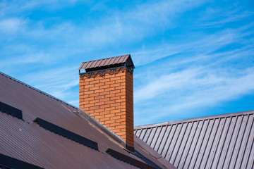 Brick forged chimney on roof of house in the sunlight. Clear blue sky background