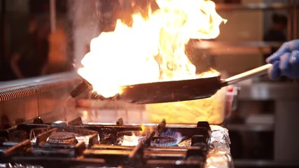 Chef is holding pan or wok and stirring or cooking with fire or flames - Powered by Adobe