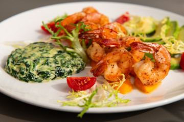 Healthy shrimp dish. Delicious grilled shrimps with avocado and salad on a white plate. Food decorated with cherry tomatoes. Sunlight. Closeup.