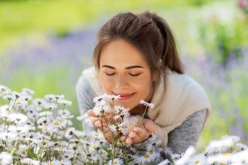 gardening and people concept - close up of happy young woman smelling chamomile flowers at summer garden