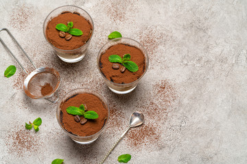 Obraz na płótnie Canvas Classic tiramisu dessert in a glass cup and strainer with cocoa powder on concrete background