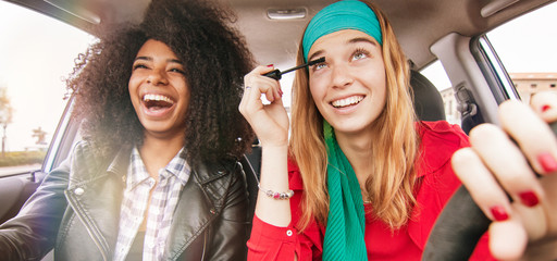 fun in car girl friends driving having fun and laughing. concept of reckless driving woman doing make up while driving with afro hair girl on passenger seat - obrazy, fototapety, plakaty