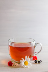 tea in a mug with berries and chamomile on a white background