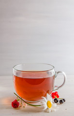 tea in a mug with berries and chamomile on a white background