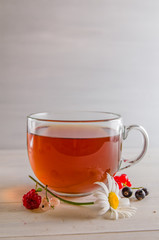 tea in a mug with berries and chamomile on a white background