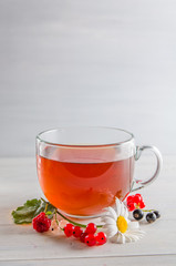tea in a mug with berries and chamomile on a white background