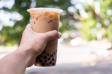 Ice milk tea with bubble boba in plastic glass in hand blur background are green tree and leaf, Taiwan ice milk tea fresh drink 
