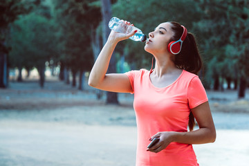woman drinking water from a bottle and listening to music while exercising